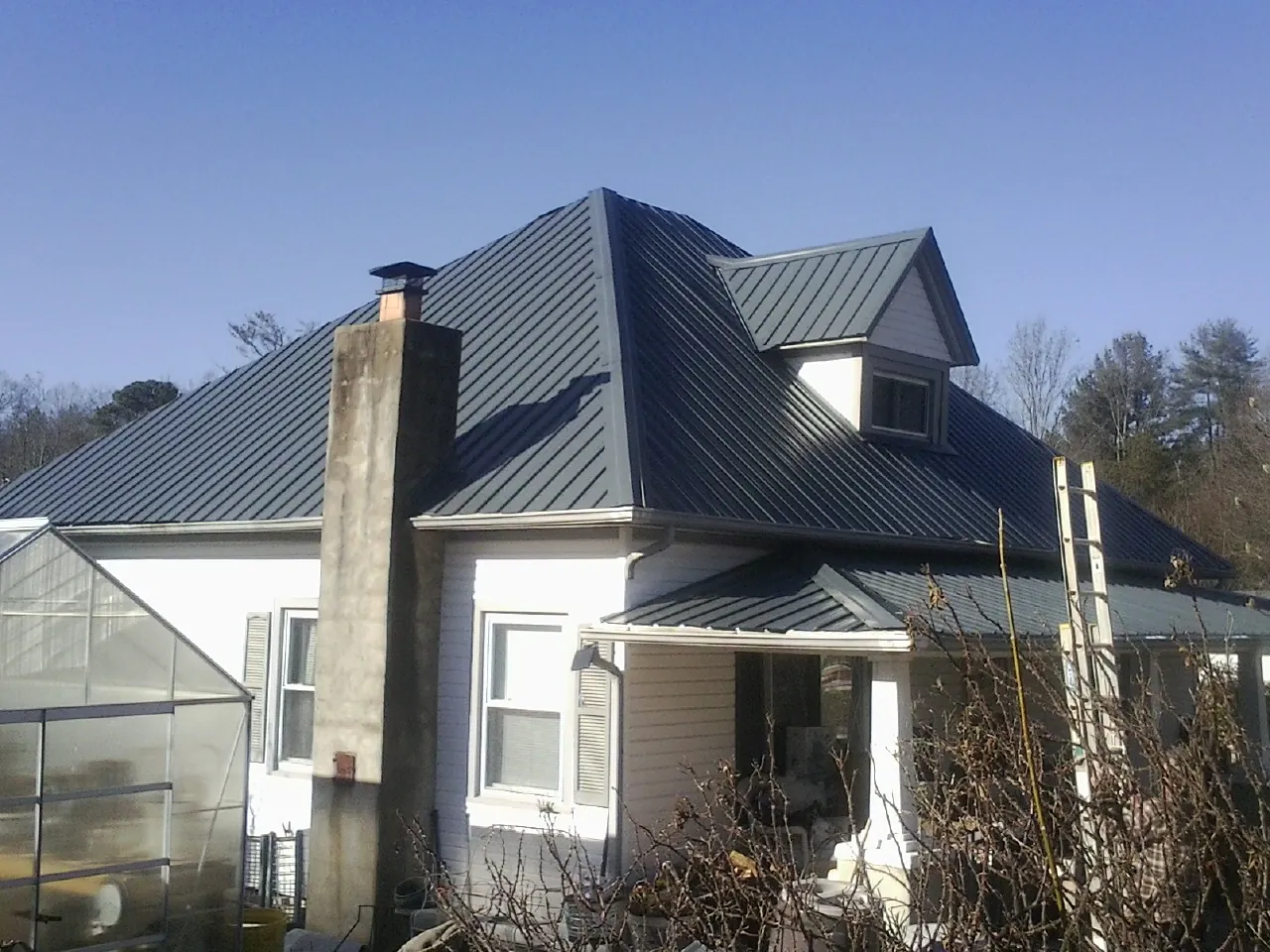 Dark blue standing seam metal roof on a white farmhouse with dormer — Slate & Tile Roof Repair by Roofing Brothers in Enderlin