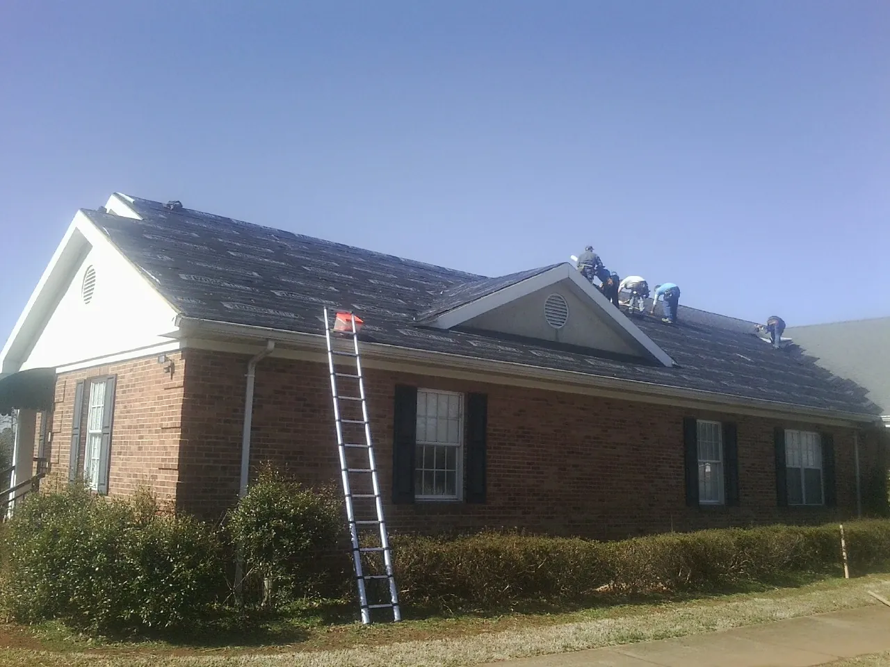 Crew tearing shingles off a brick ranch roof with a ladder set — Emergency Roof Repair work by our crew in Enderlin
