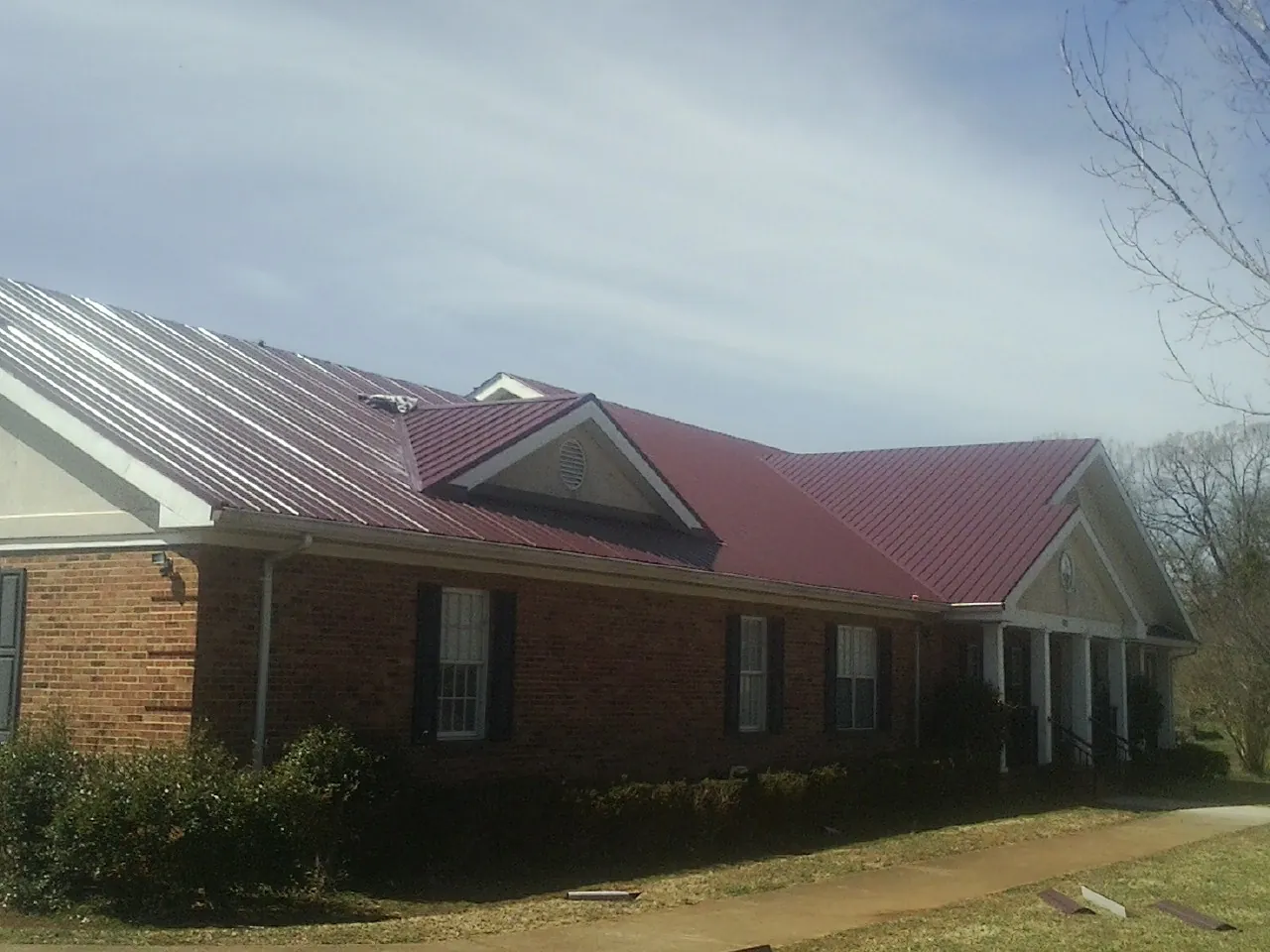 Red metal roof with gabled entries on a long brick building, from a Hail Damage Roof Repair job in Enderlin