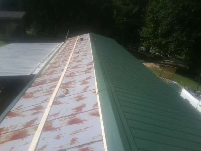 Old rusted panels beside newly installed green metal roofing — Wind Damage Roof Repair by Roofing Brothers in Enderlin