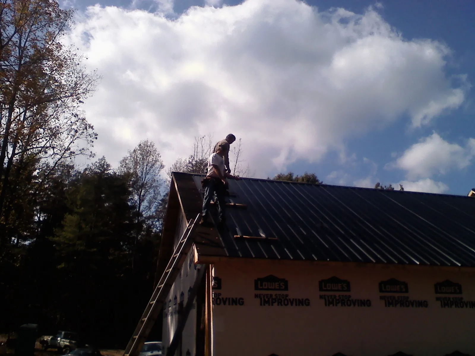 Roofer fastening dark metal panels high against a cloudy sky, from a Roof Inspection job in Enderlin