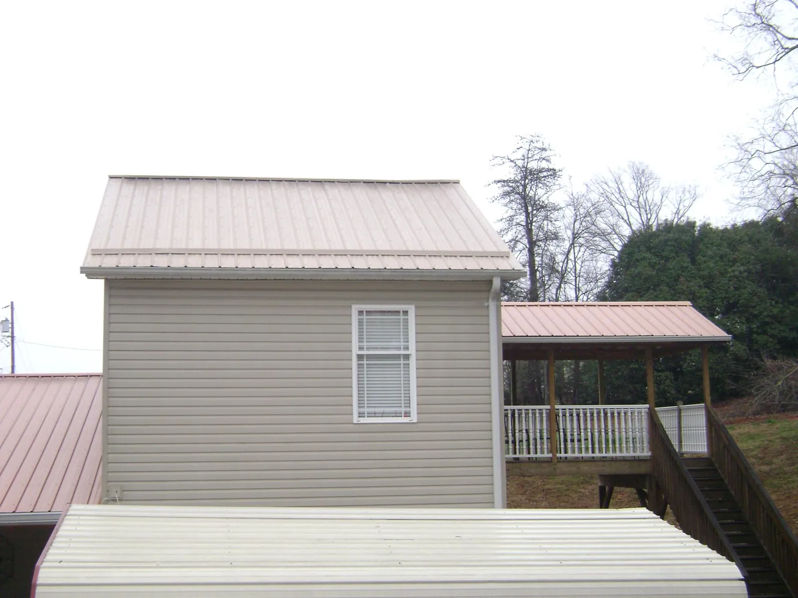 Tan metal roofs on a two story addition and attached porch, from a Roof Replacement job in Enderlin
